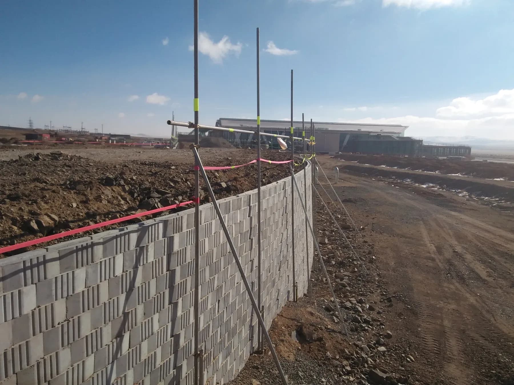 Modular block wall part-built, with the reinforced fill behind it placed to the height of the last course.