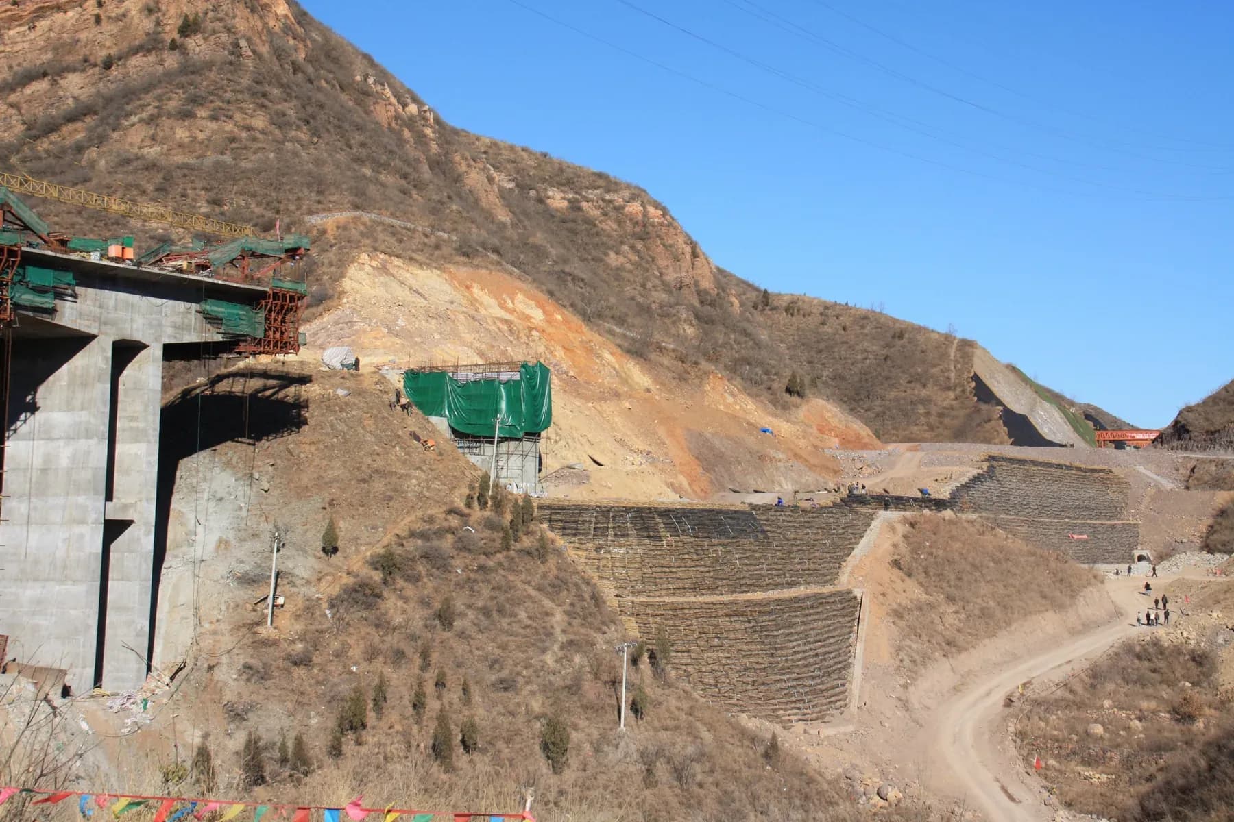 Reinforced soil slope under construction on steep terrain, carrying an approach embankment towards a bridge.