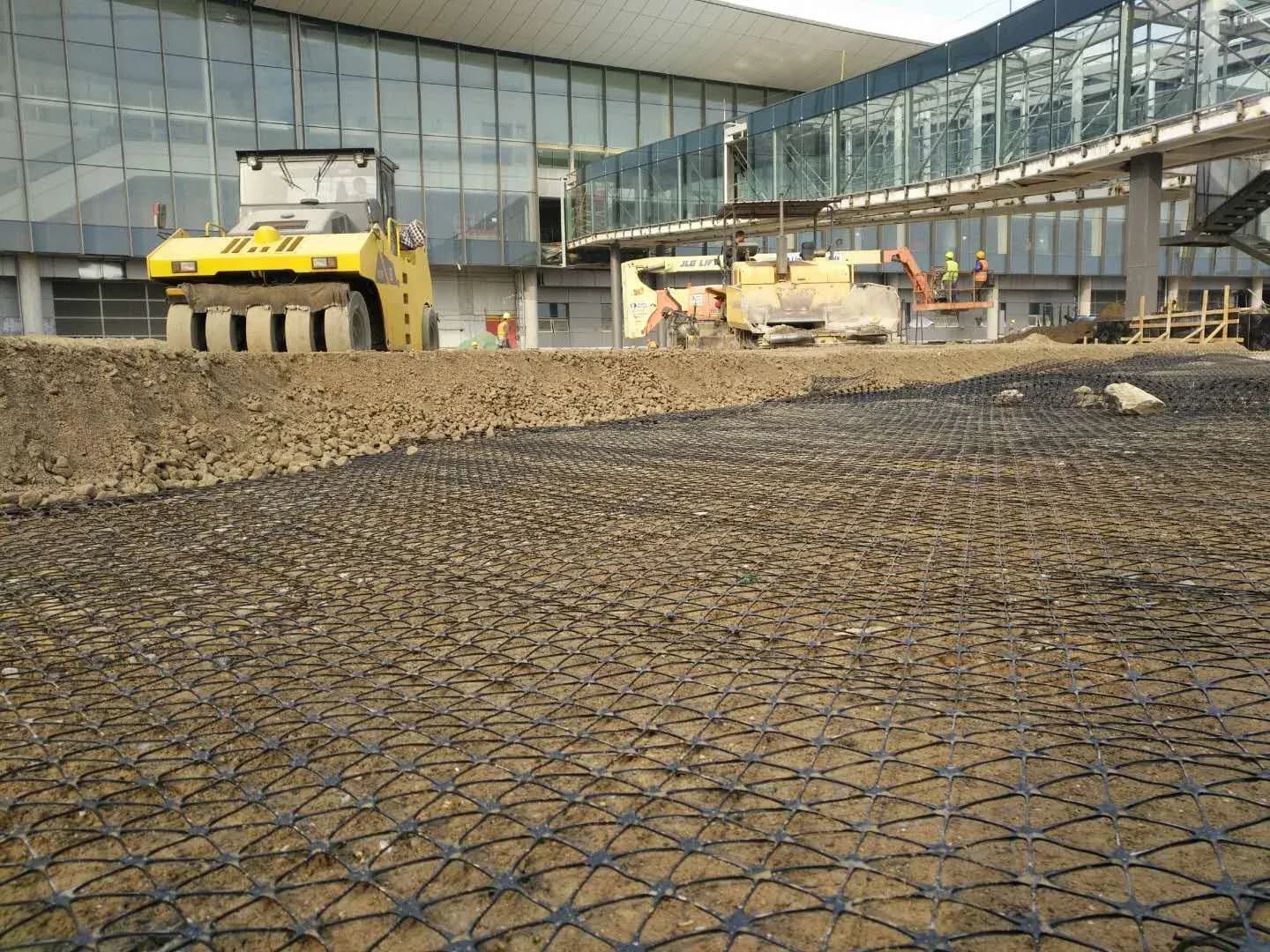 Roller compacting the granular layer over placed triaxial geogrid on a working platform.