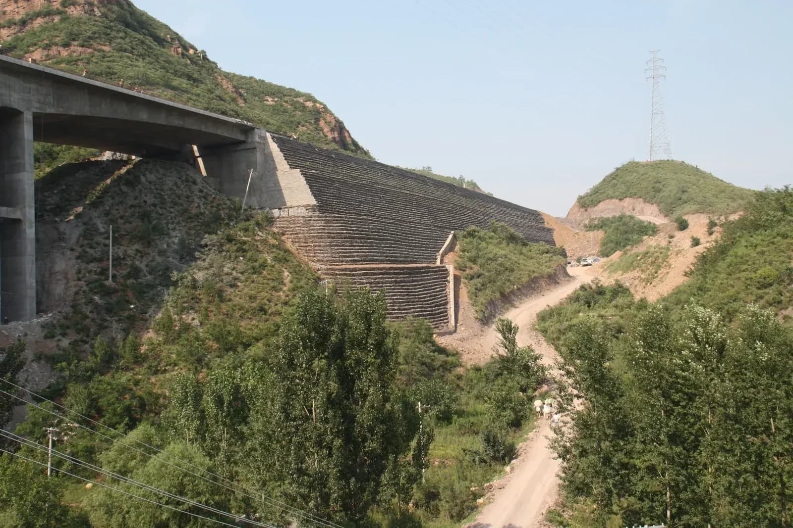 Terraced reinforced soil slope in benched lifts, carrying the approach fill beside a viaduct.