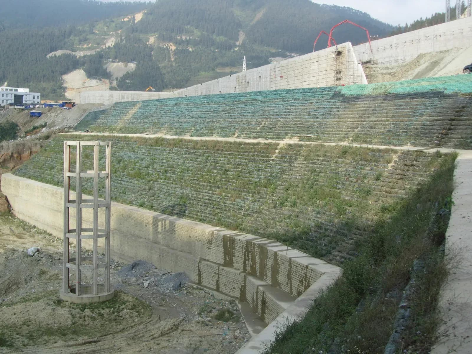 Benched reinforced soil slope with planted terraces and a concrete capping structure at the crest.